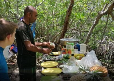 Guide de TamTam Pagaie et jeune participant préparant un déjeuner de style créole sur une table de camping, entourés par la verdure dense de la mangrove de Guadeloupe, lors d'une randonnée en kayak.